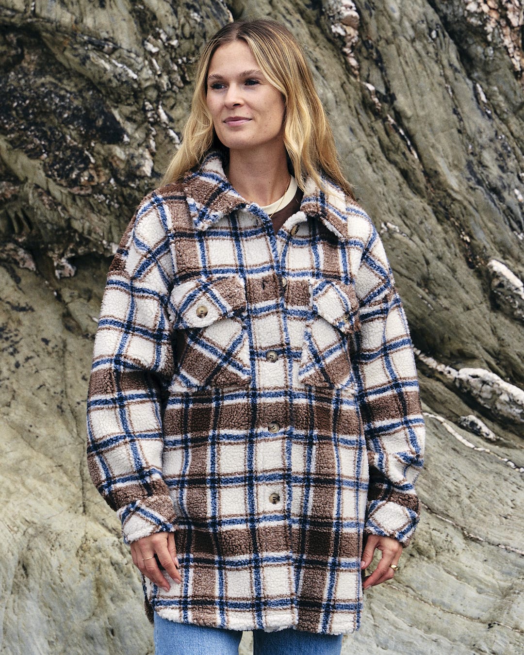 A woman wearing a Laurie - Womens Check Sherpa Fleece Coat - Cream by Saltrock standing in front of rocks.