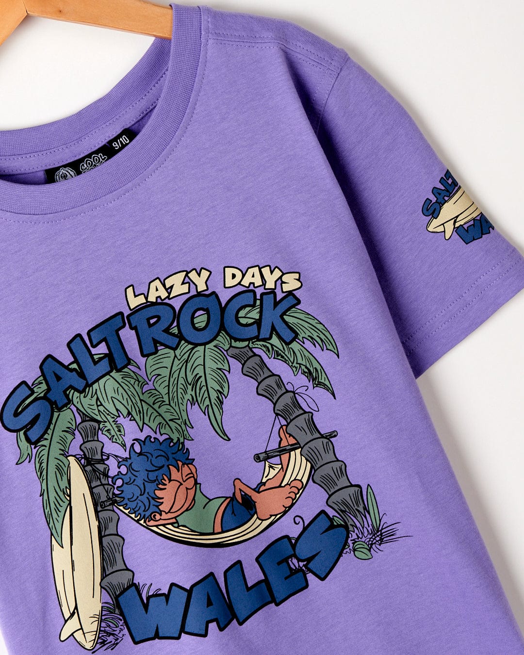 A purple, cotton material t-shirt with a graphic of a person lounging in a hammock and the text "Saltrock Wales, Lazy Days" displayed on the front.