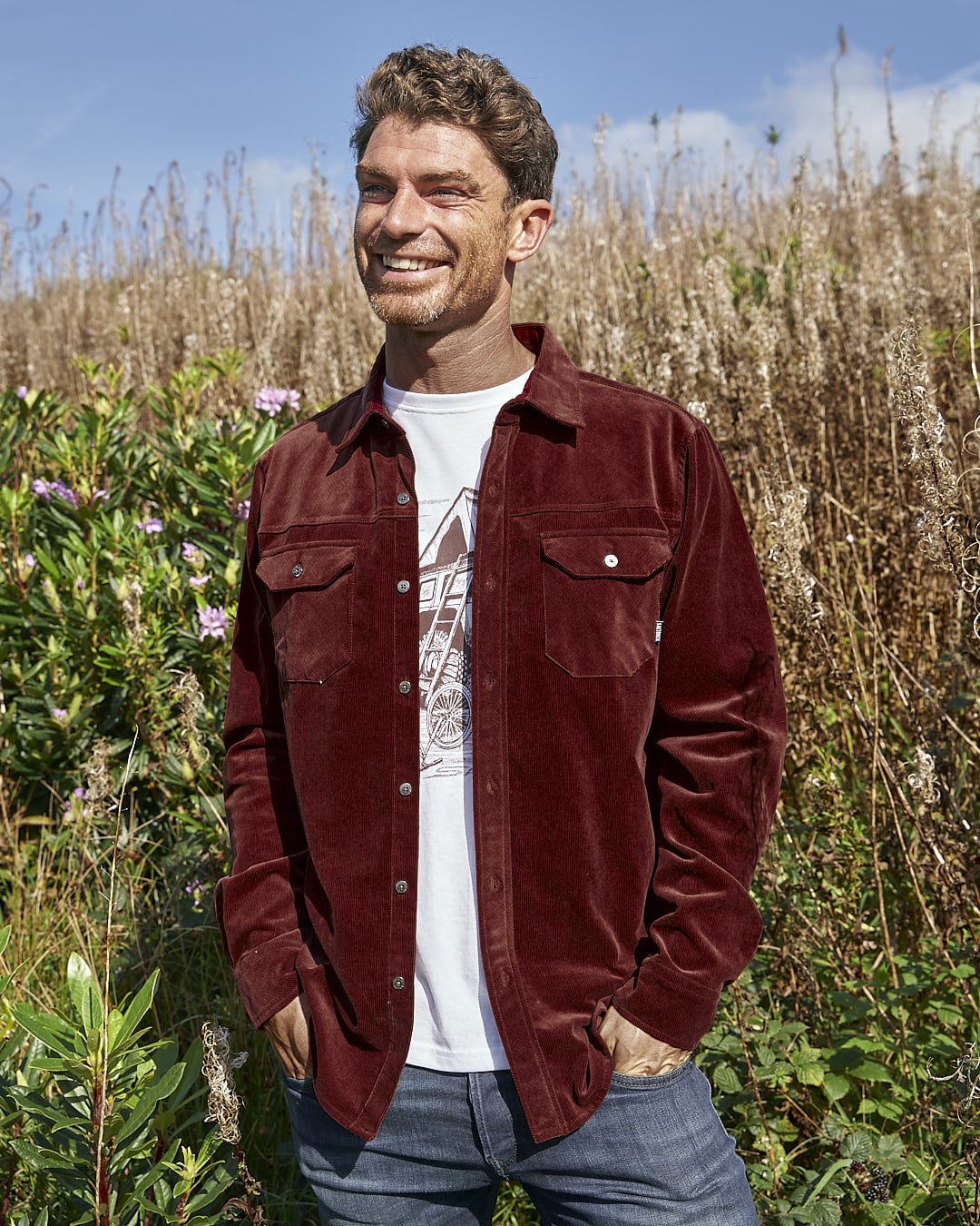 A man standing in a field wearing a Saltrock Linus - Mens Long Sleeve Shirt - Dark Red.