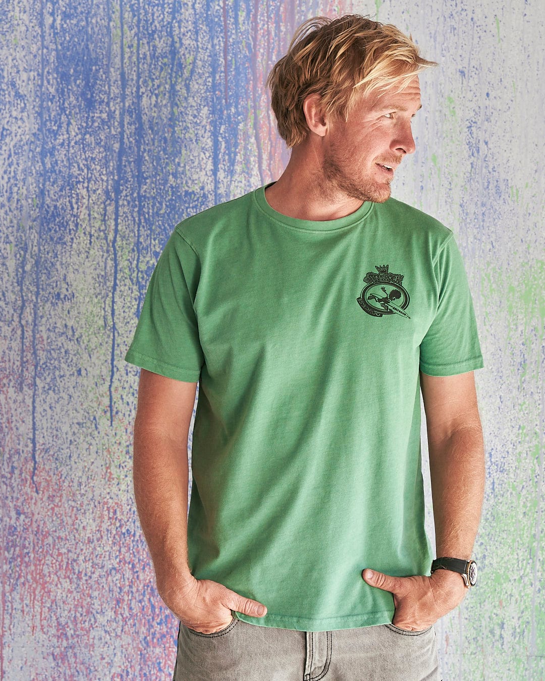 A man wearing a Little Creatures - Limited Edition 35 Years T-Shirt by Saltrock standing in front of a colorful wall.