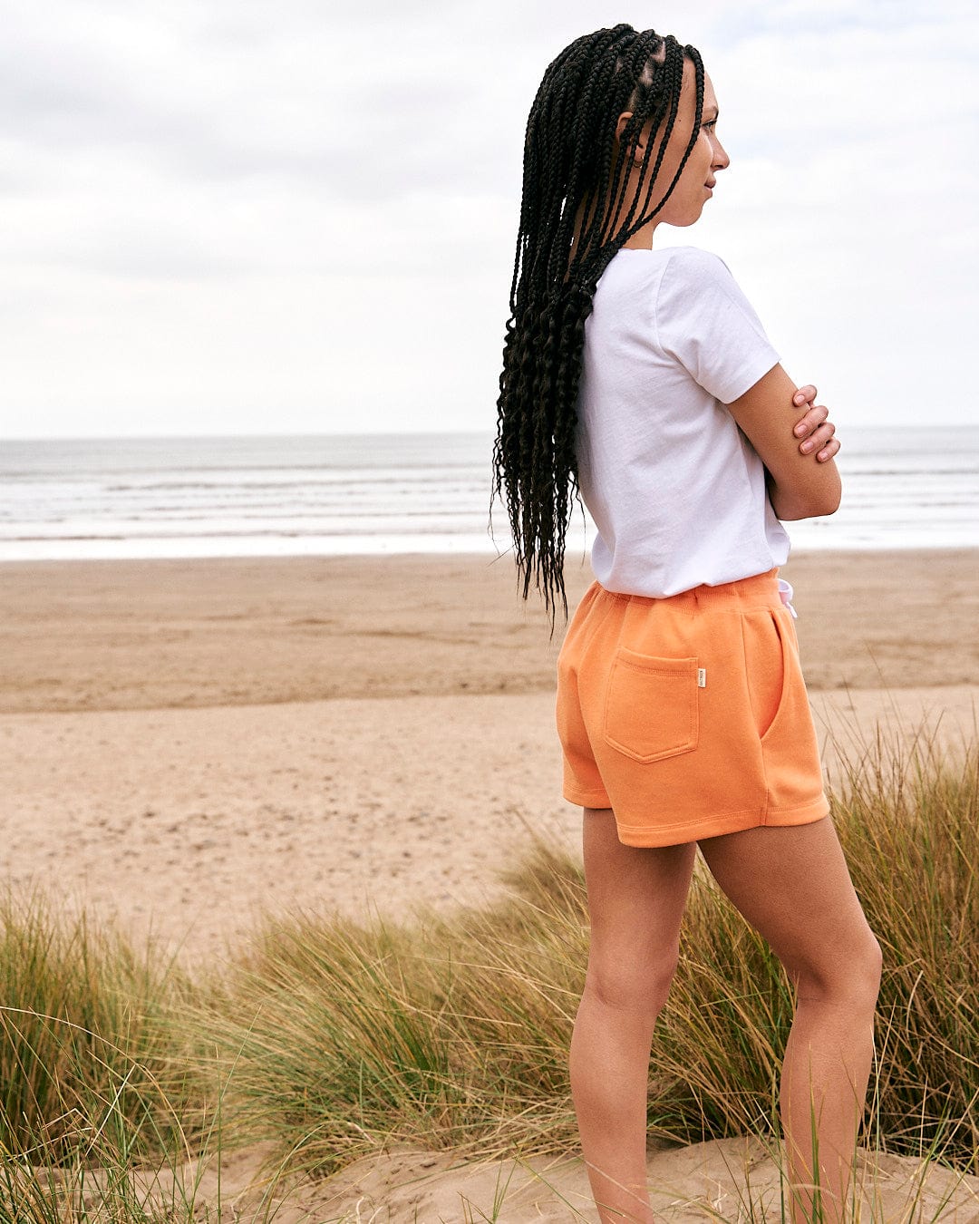 A woman in orange shorts standing on a beach wearing the Love Your Ocean - Womens Short Sleeve T-Shirt in White by Saltrock.