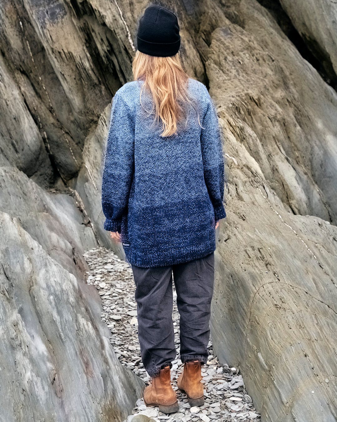 A woman standing on a beach wearing a Saltrock Lynton - Womens Button Cardigan - Dark Blue and boots.