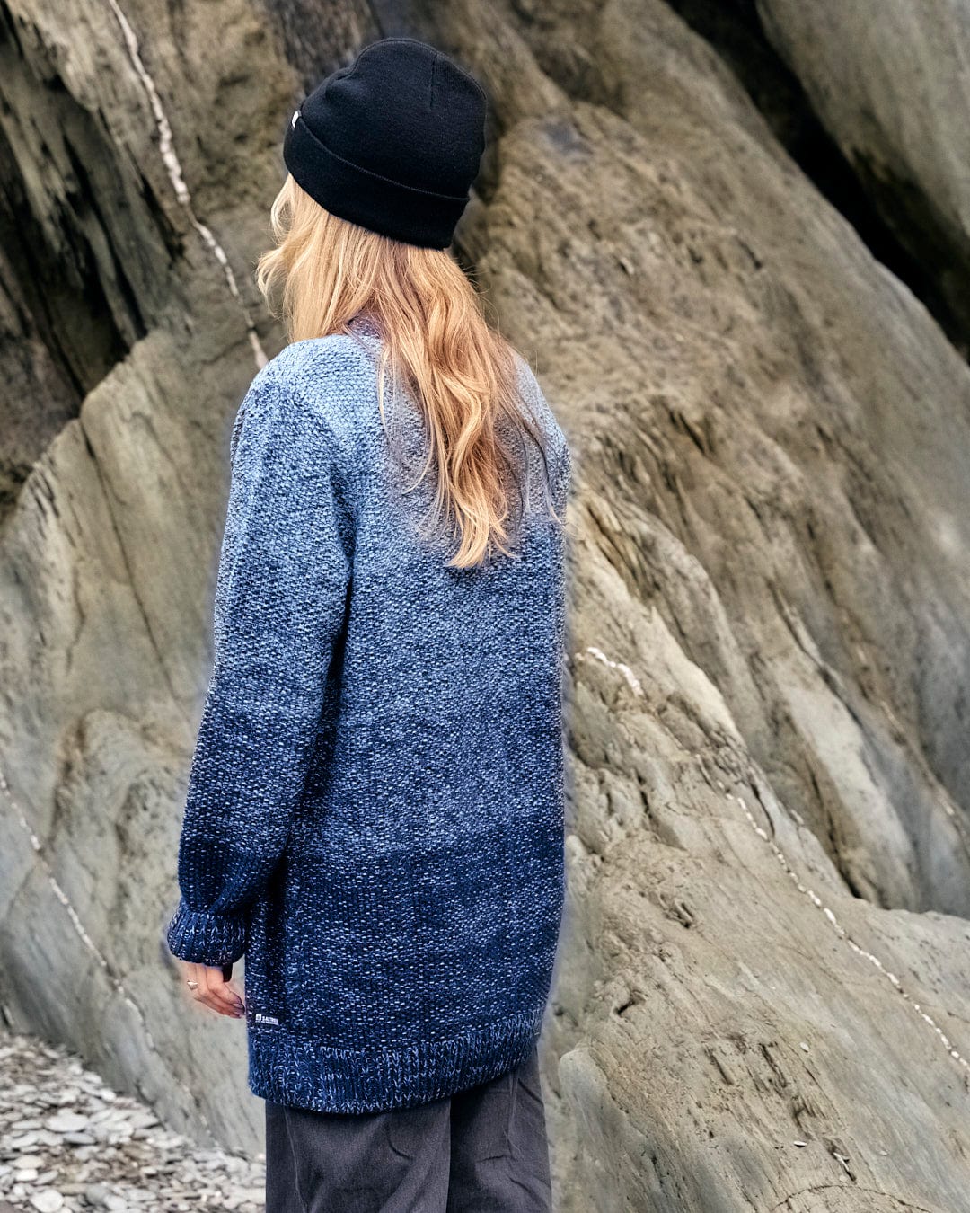 A woman wearing a Saltrock Lynton - Womens Button Cardigan - Dark Blue standing on rocks.