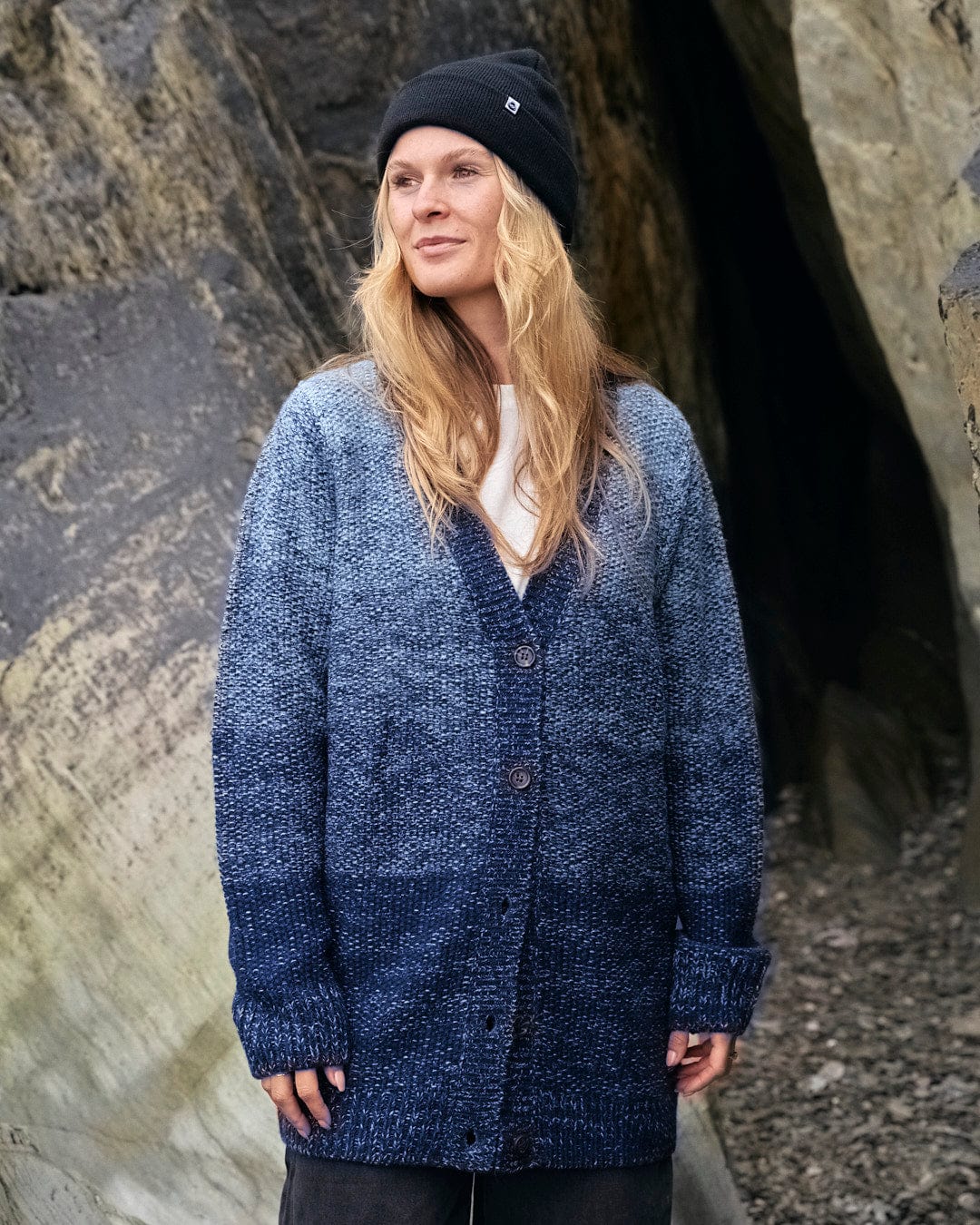 A woman wearing a Saltrock Lynton - Womens Button Cardigan - Dark Blue standing in front of rocks.