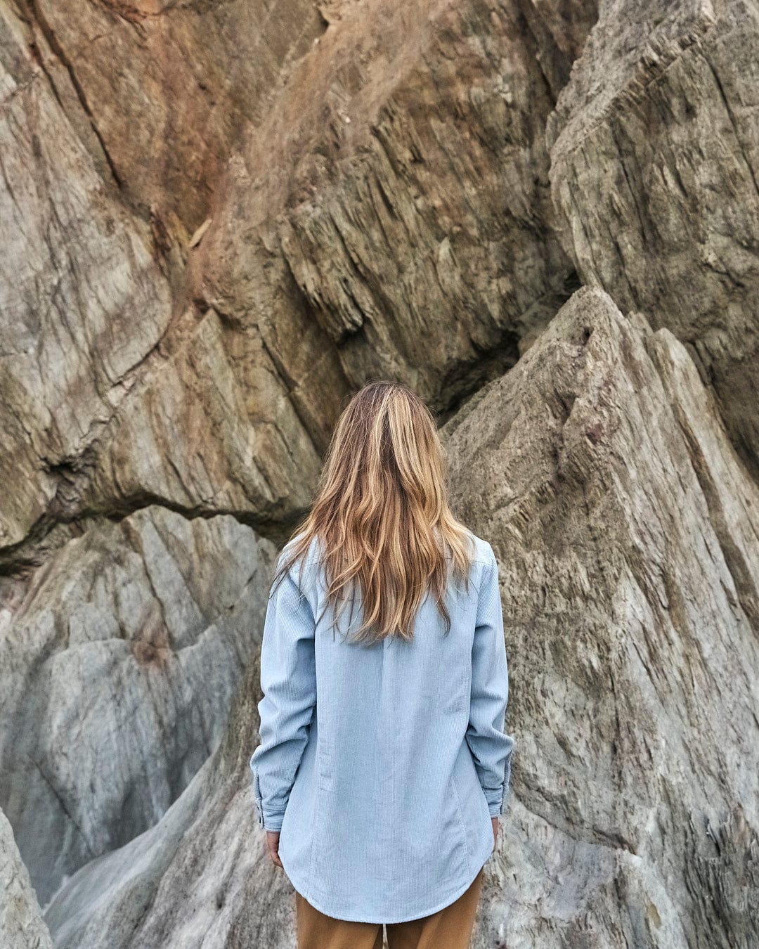 A woman wearing a Saltrock Maddox Shirt with buttoned cuffs posing in front of rocks, showcasing Saltrock branding.