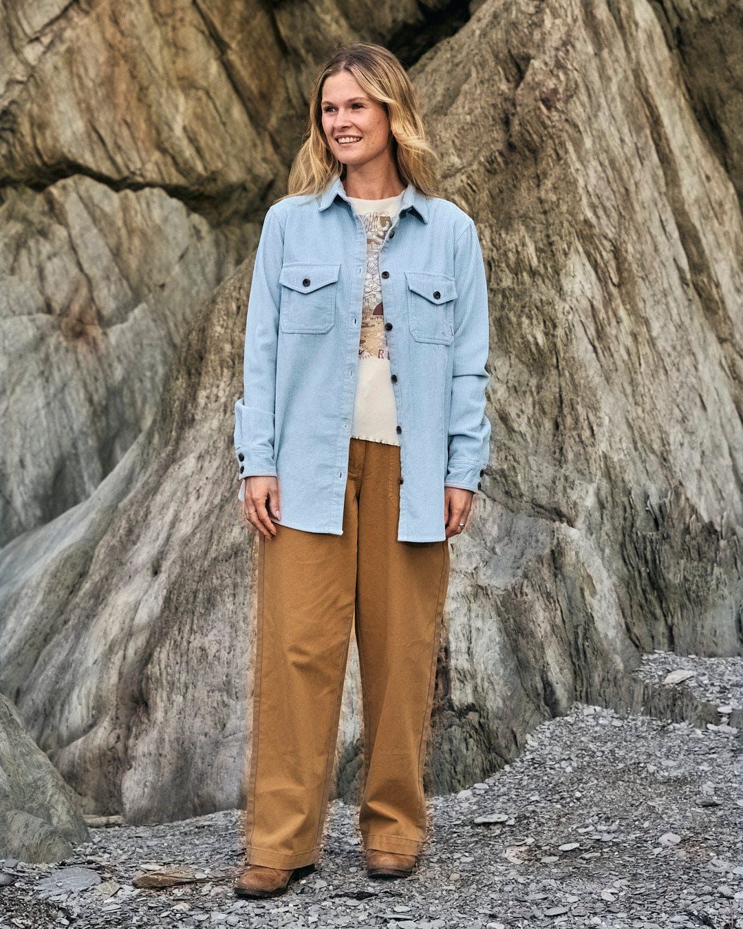 A woman is standing in front of rocks wearing a blue Saltrock Maddox - Womens Cord Shirt - Light Blue.