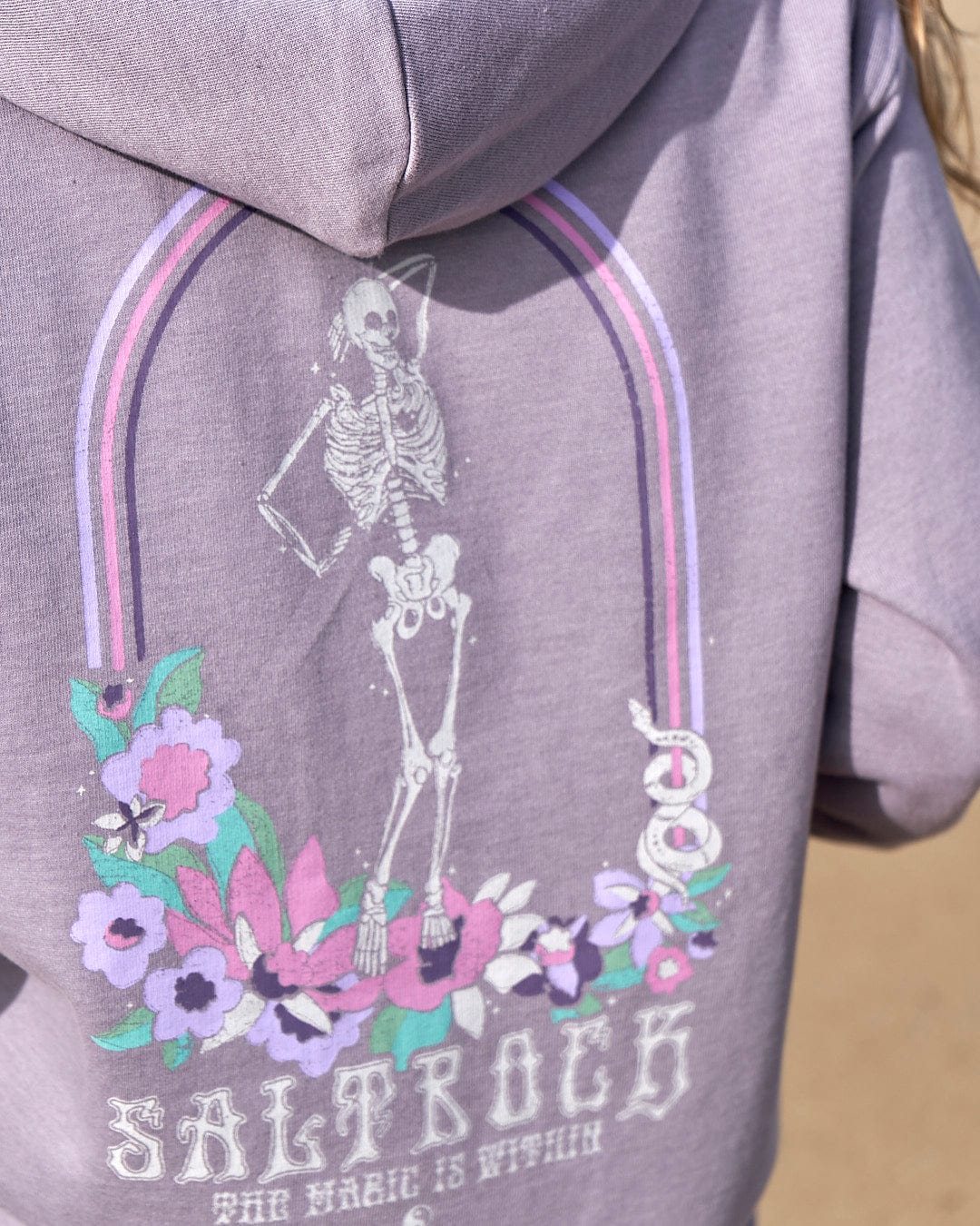 A girl wearing a Magic Within - Womens Zip Hoodie - Lilac by Saltrock with a floral skeleton design.