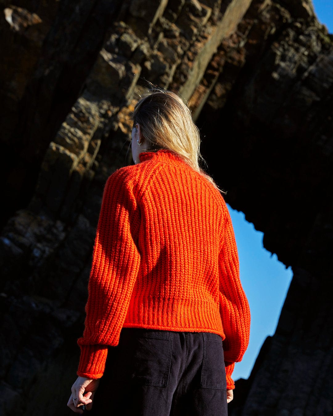 A woman in a Saltrock Mandy - Womens Funnel Neck Jumper - Red standing in front of a rock.