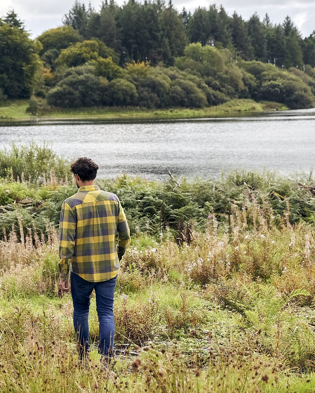A man wearing Saltrock's Mattie - Mens Long Sleeve Shirt - Yellow is walking through tall grass near a lake.
