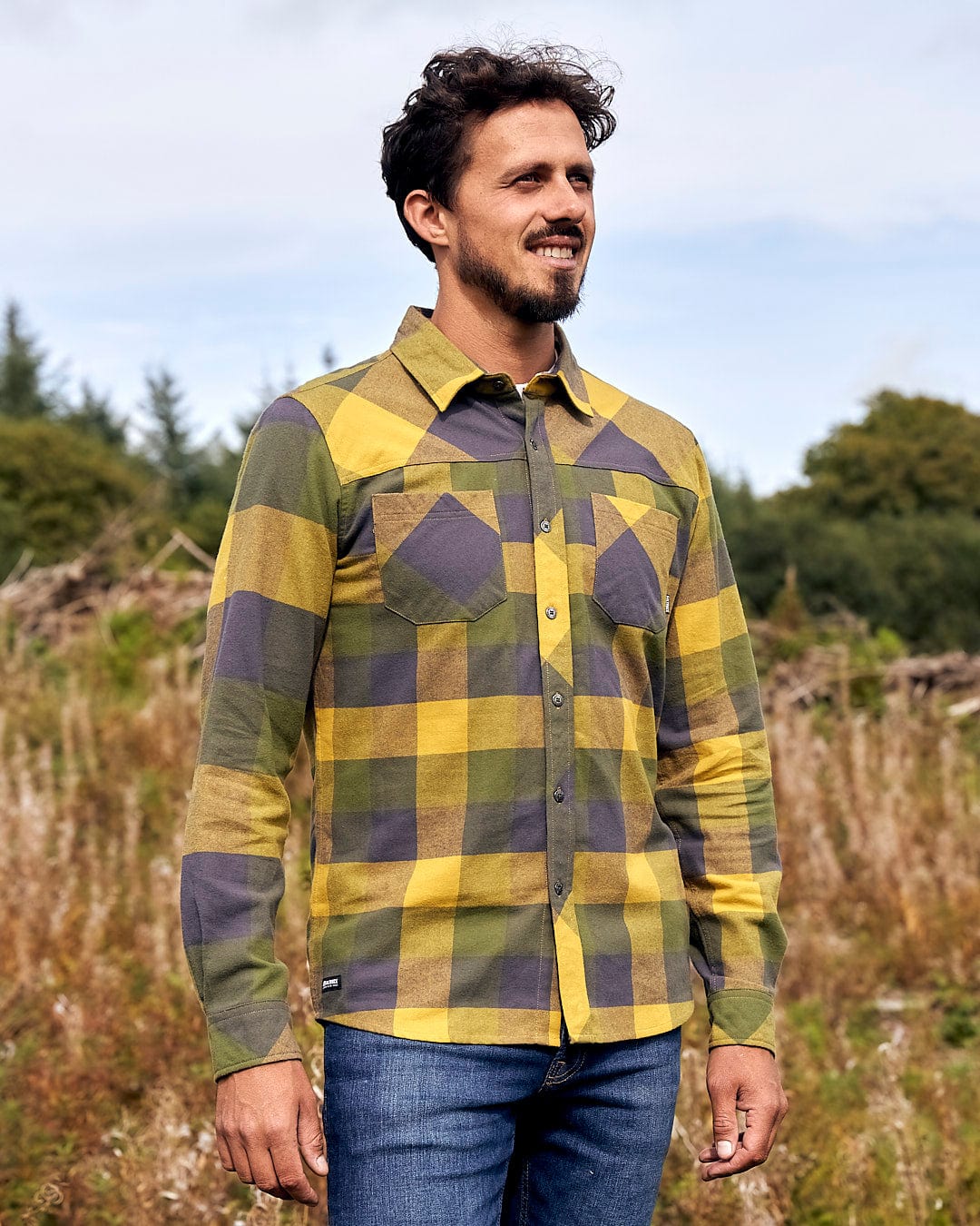 A man is standing in a field wearing a Saltrock Mattie - Mens Long Sleeve Shirt - Yellow and grey plaid shirt.