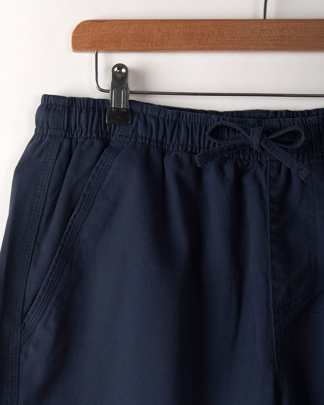 Close-up of Saltrock Meddon men's chino shorts in blue, featuring an elasticated waistband and front pockets, hanging on a wooden hanger.