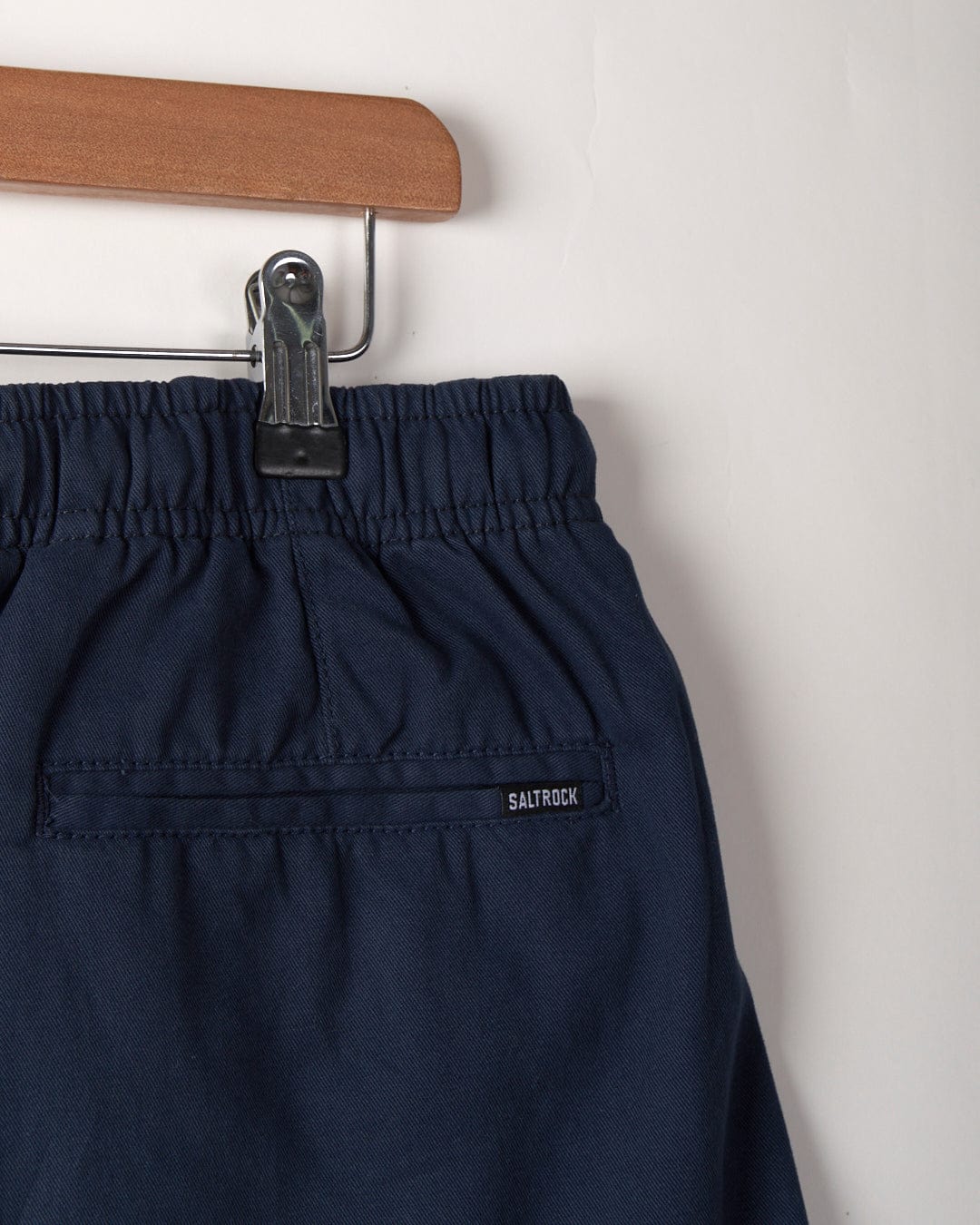 Close-up of Saltrock’s Meddon Men's Chino Shorts in blue, featuring a relaxed fit and elasticated waist, hanging on a wooden hanger with the Saltrock label visible above the back pocket.