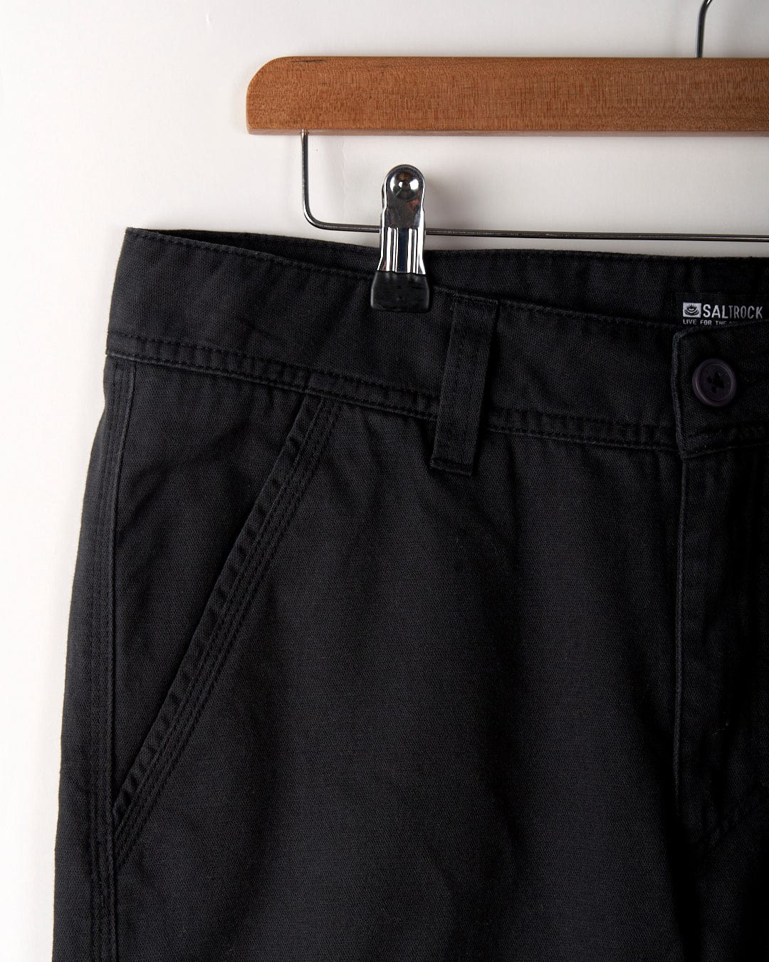 Close-up of the waistband, button, and front pocket of the Saltrock Meltan Men's Straight Leg Twill Trouser in dark grey, displayed on a wooden hanger.