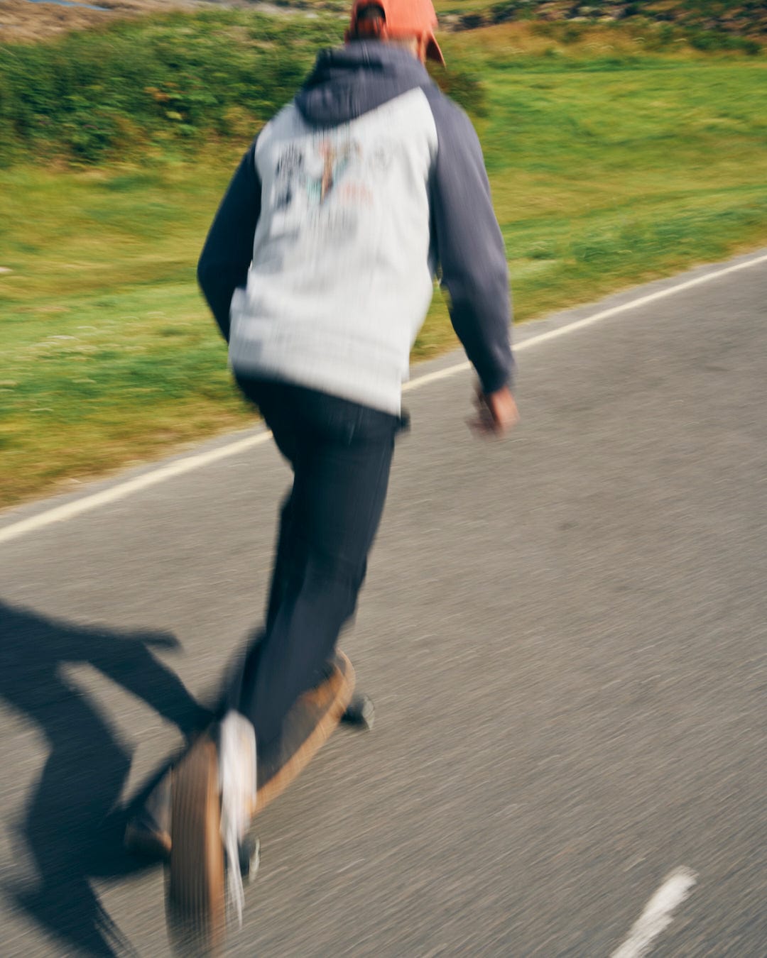 A person in Saltrock Meltan Men's Straight Leg Twill Trousers (Dark Grey) rides a skateboard on a paved park path, captured with motion blur.