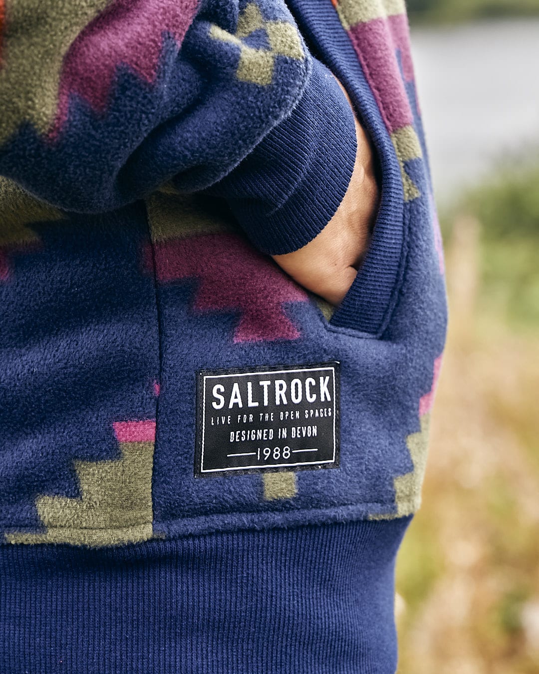 The back of a man wearing a Saltrock Merida - Womens Lined Aztec Zip Fleece - Dark Blue hoodie.