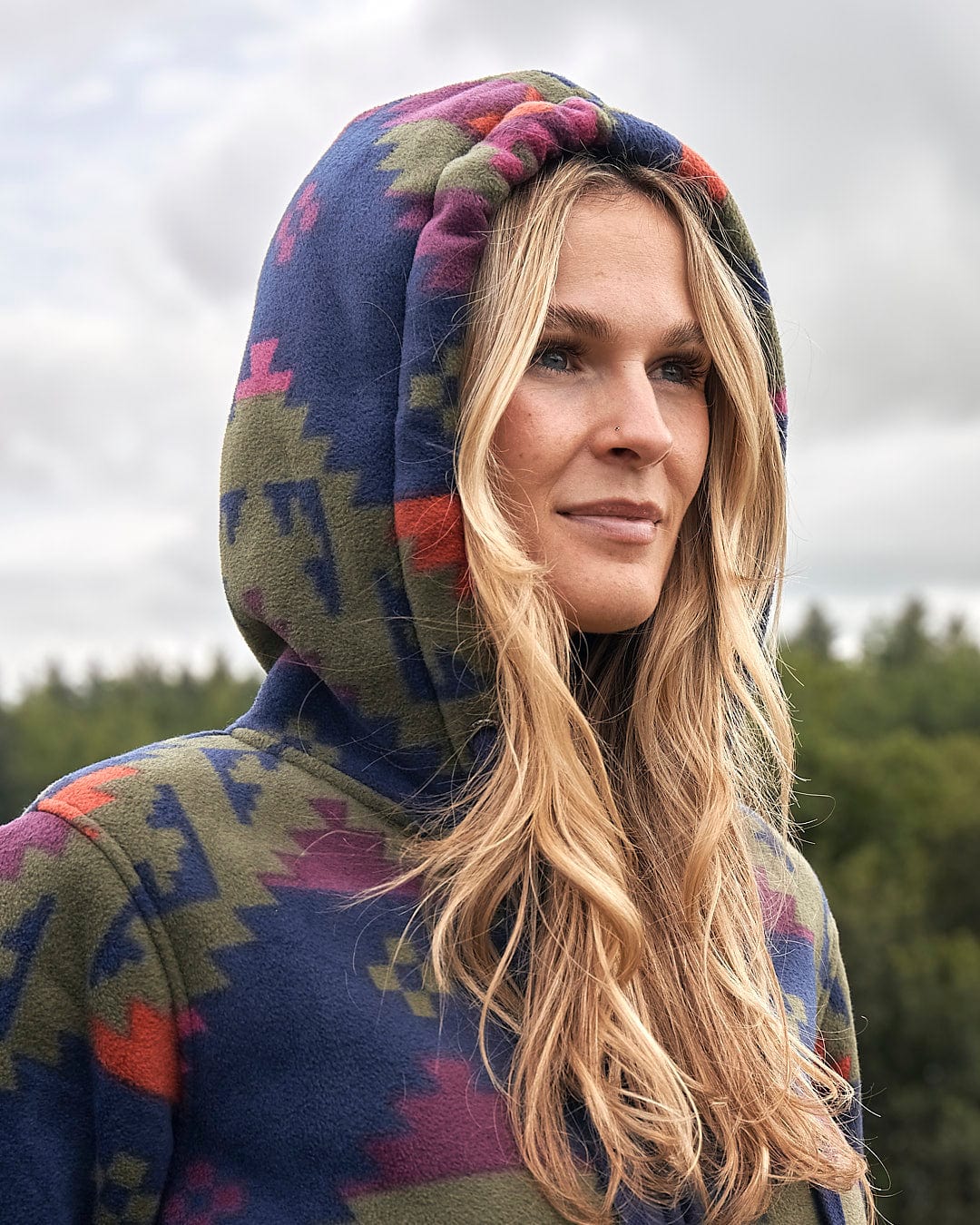 A woman in a colorful hoodie standing in a field wearing the Saltrock Merida - Womens Lined Aztec Zip Fleece - Dark Blue.