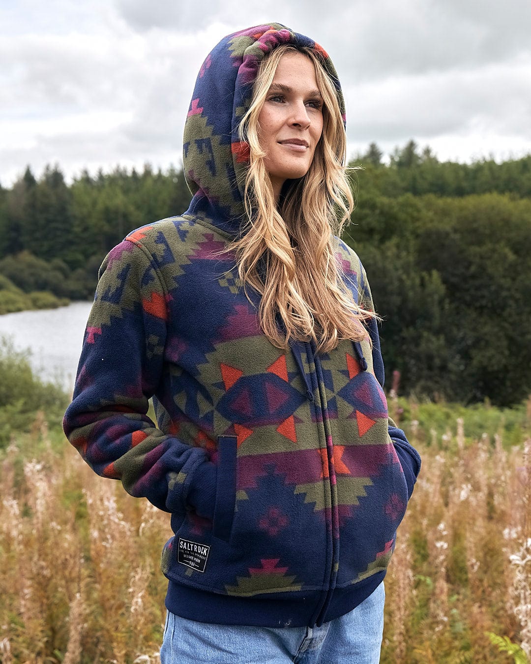 A woman is standing in a field wearing a Saltrock Merida - Womens Lined Aztec Zip Fleece - Dark Blue.