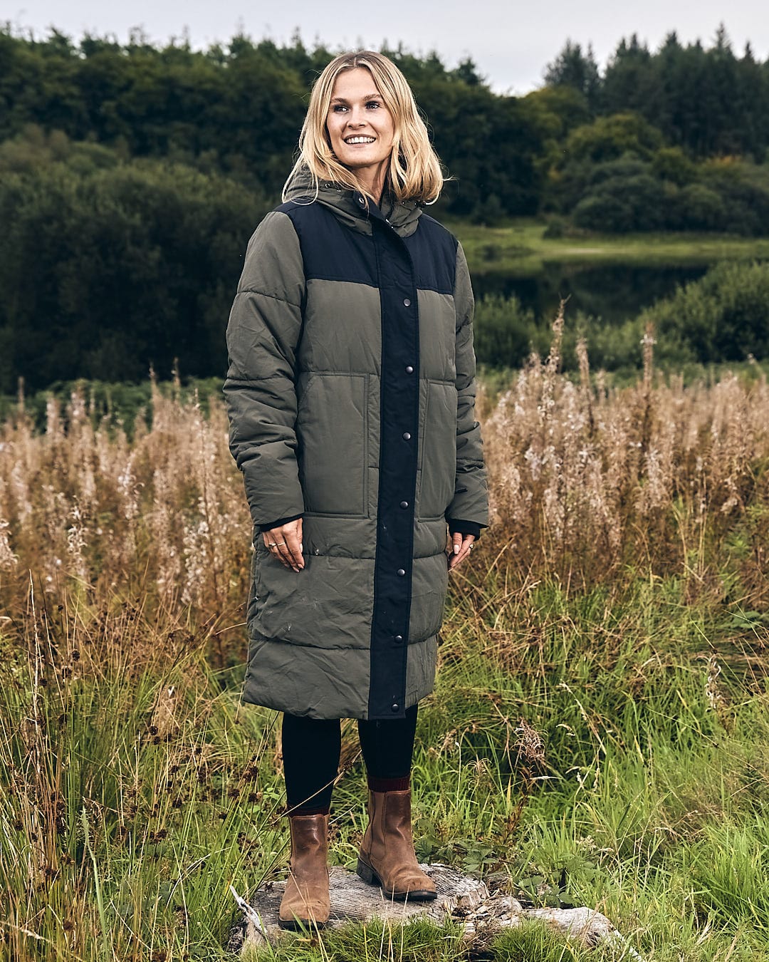 A woman standing in a field wearing a Saltrock Merle - Womens Puffer Jacket - Dark Green.