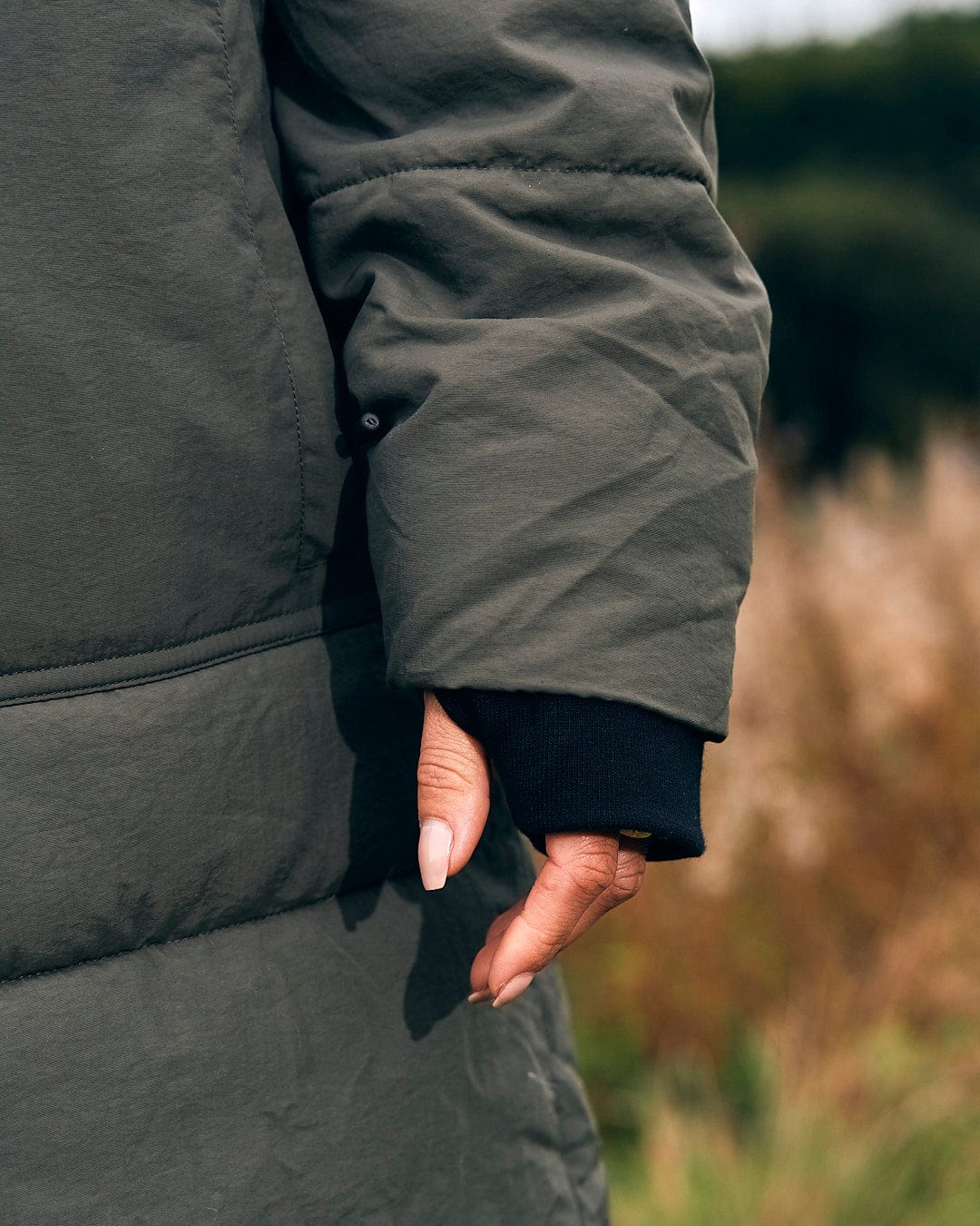 A woman's hand in a Saltrock Merle - Womens Puffer Jacket - Dark Green in a field.