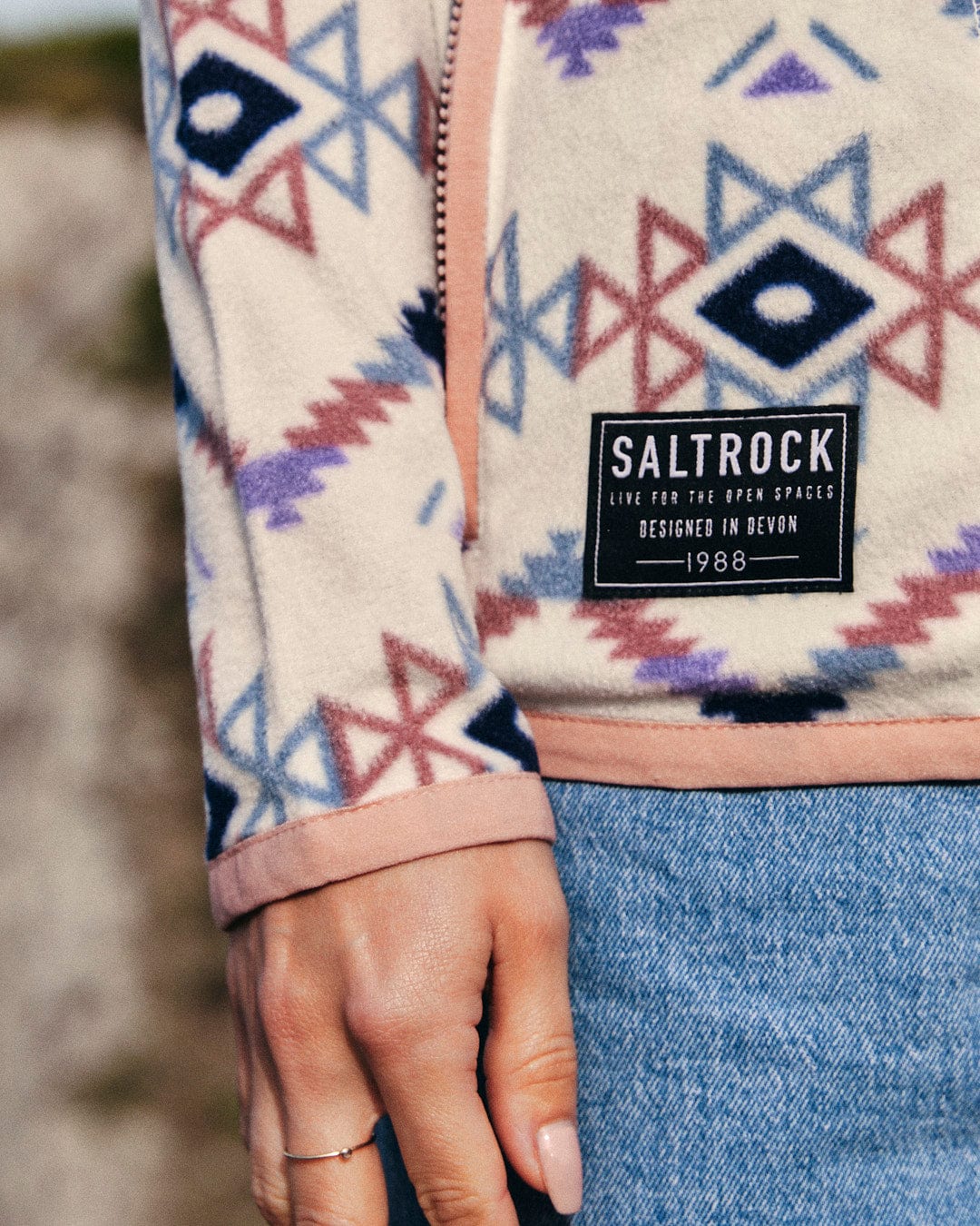 A woman's hand is holding a Micro Ida - Womens Zip Fleece - Cream with the Saltrock branding on it.