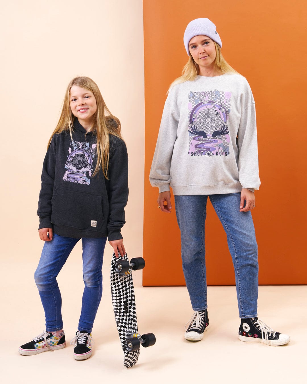 A girl and a boy standing next to a Saltrock skateboard showcasing a colourful graphic design.