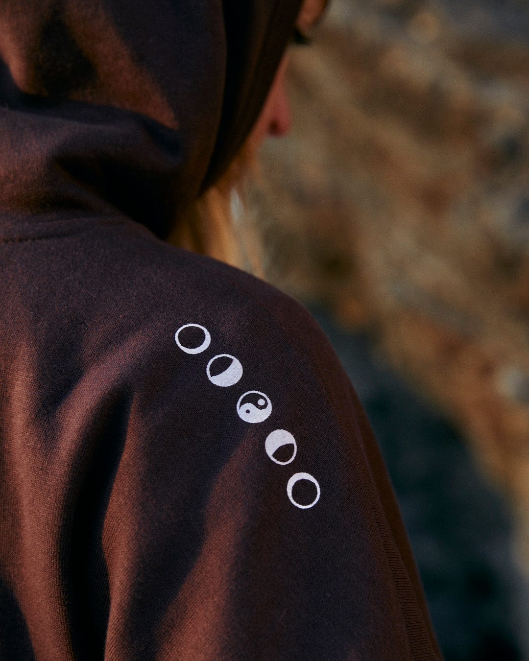 The back of a woman wearing a Saltrock branded Mocha - Womens Pop Hoodie - Brown, combining style and comfort, adorned with the phases of the moon.