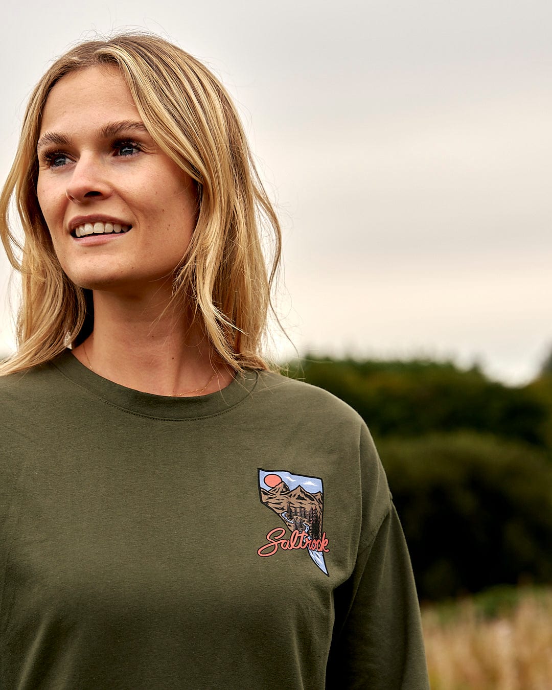 A woman wearing a Saltrock Mountain Creek - Womens Long Sleeve T-Shirt - Green standing in a field.