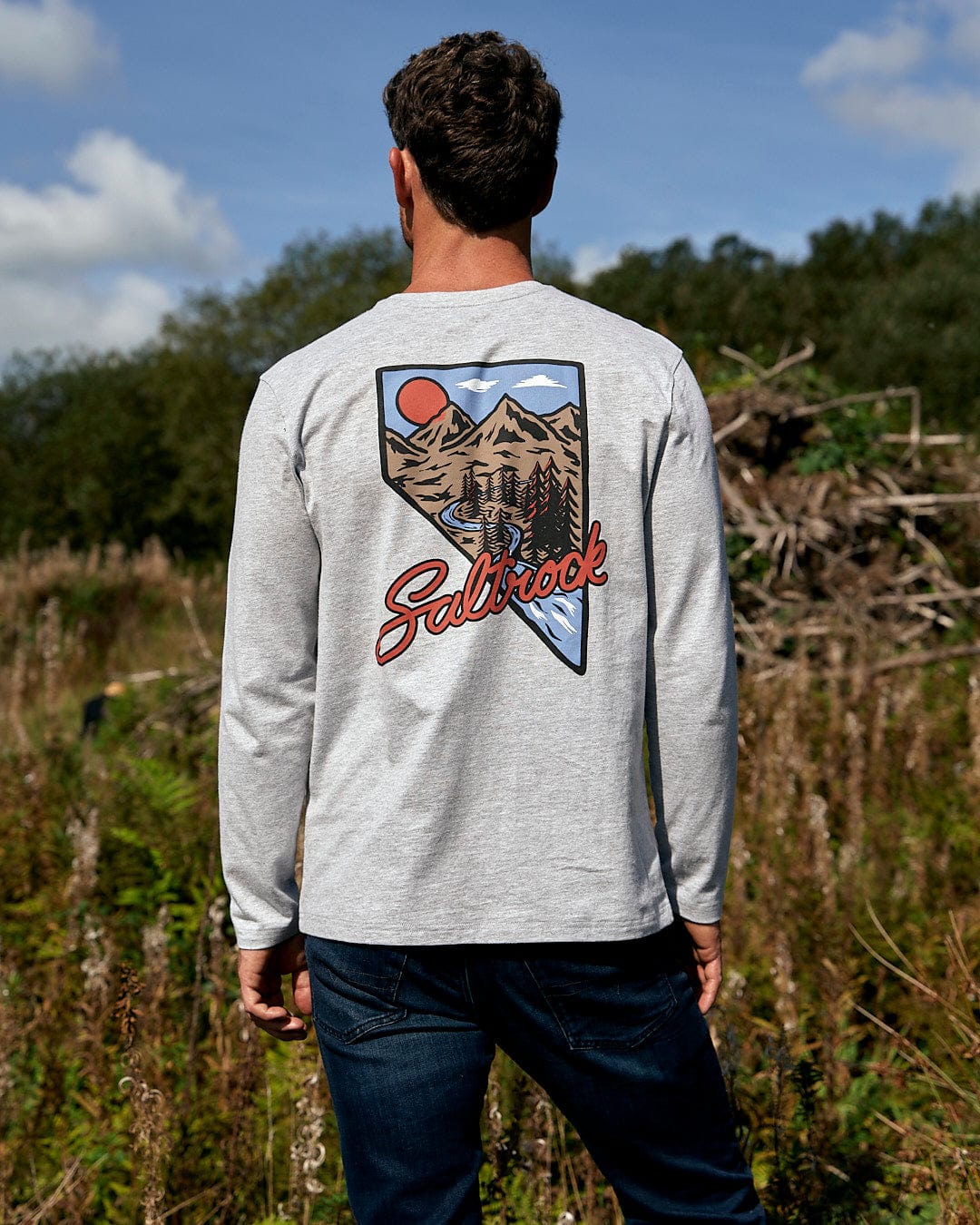 A man standing in a field wearing a Saltrock Mountain Creek - Mens Long Sleeve T-Shirt - Grey.