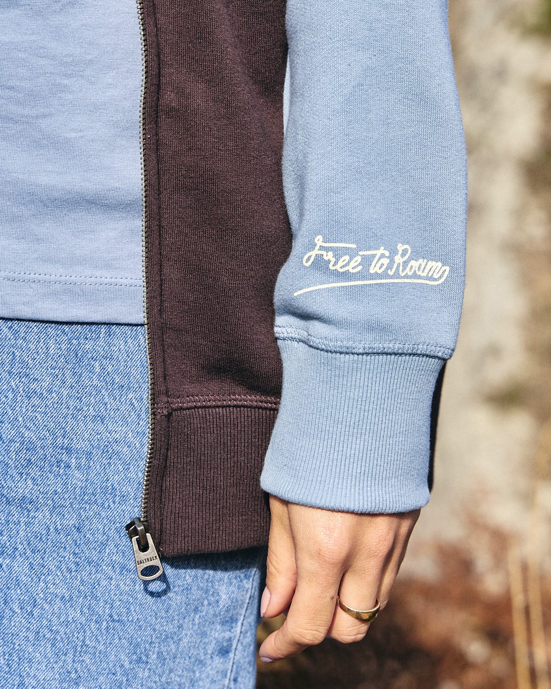 An adventurous woman wearing a blue Saltrock Mountain Roaming - Womens Raglan Zip Hoodie - Brown and jeans.