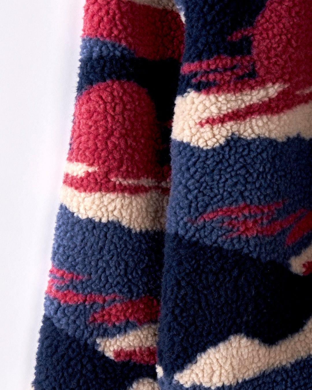 Close-up of a textured fleece fabric from the Saltrock Mountain Trail - Kids Recycled Borg Zip Fleece, showcasing a pattern of red, white, and dark blue abstract shapes reminiscent of a mountain landscape.