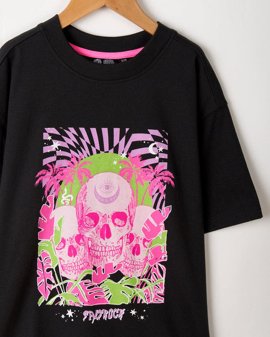 A Saltrock Mystic Skulls Kids Short Sleeve T-Shirt in Black with a pink and white skull illustration featuring tropical elements hangs against a white background.