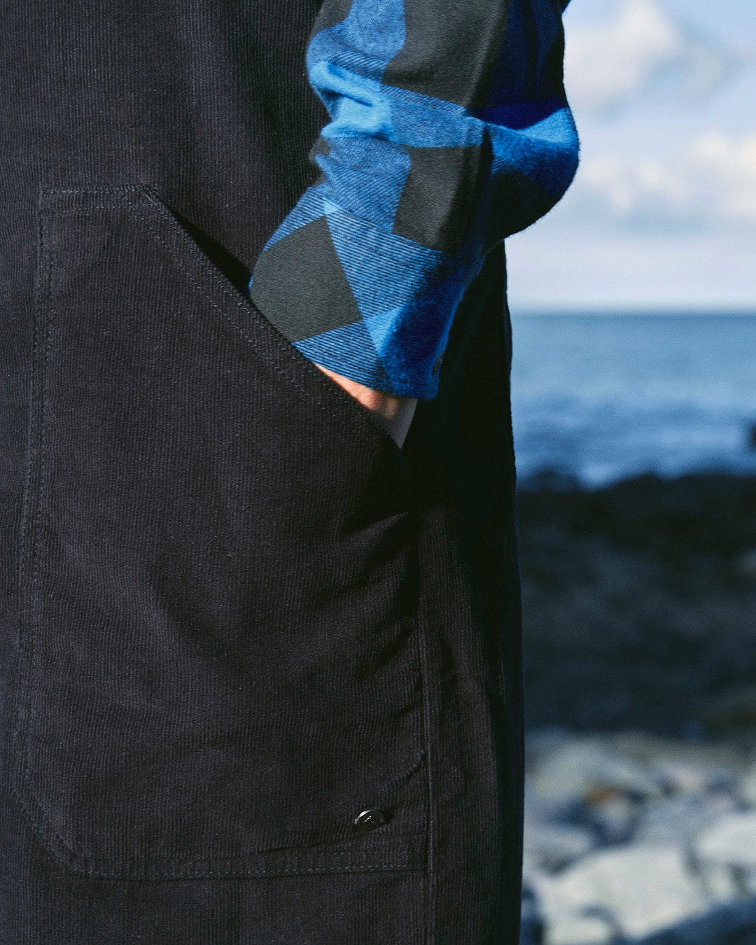 A stylish man wearing the Saltrock Nancy - Womens Cord Dungaree - Dark Blue standing next to the ocean.