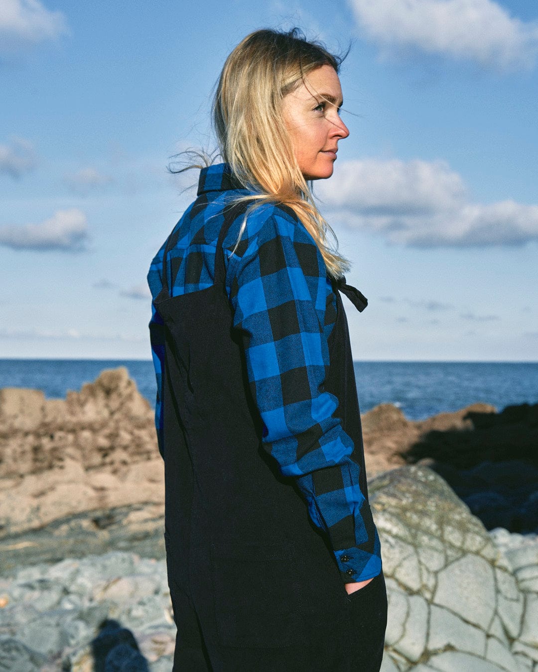 A fashion-conscious woman in a Nancy - Womens Cord Dungaree - Dark Blue by Saltrock standing on rocks by the ocean.