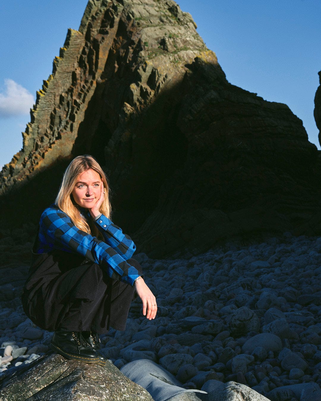 A fashion-conscious woman stylishly crouching on a rock, wearing a Saltrock Nancy - Womens Cord Dungaree - Dark Blue.