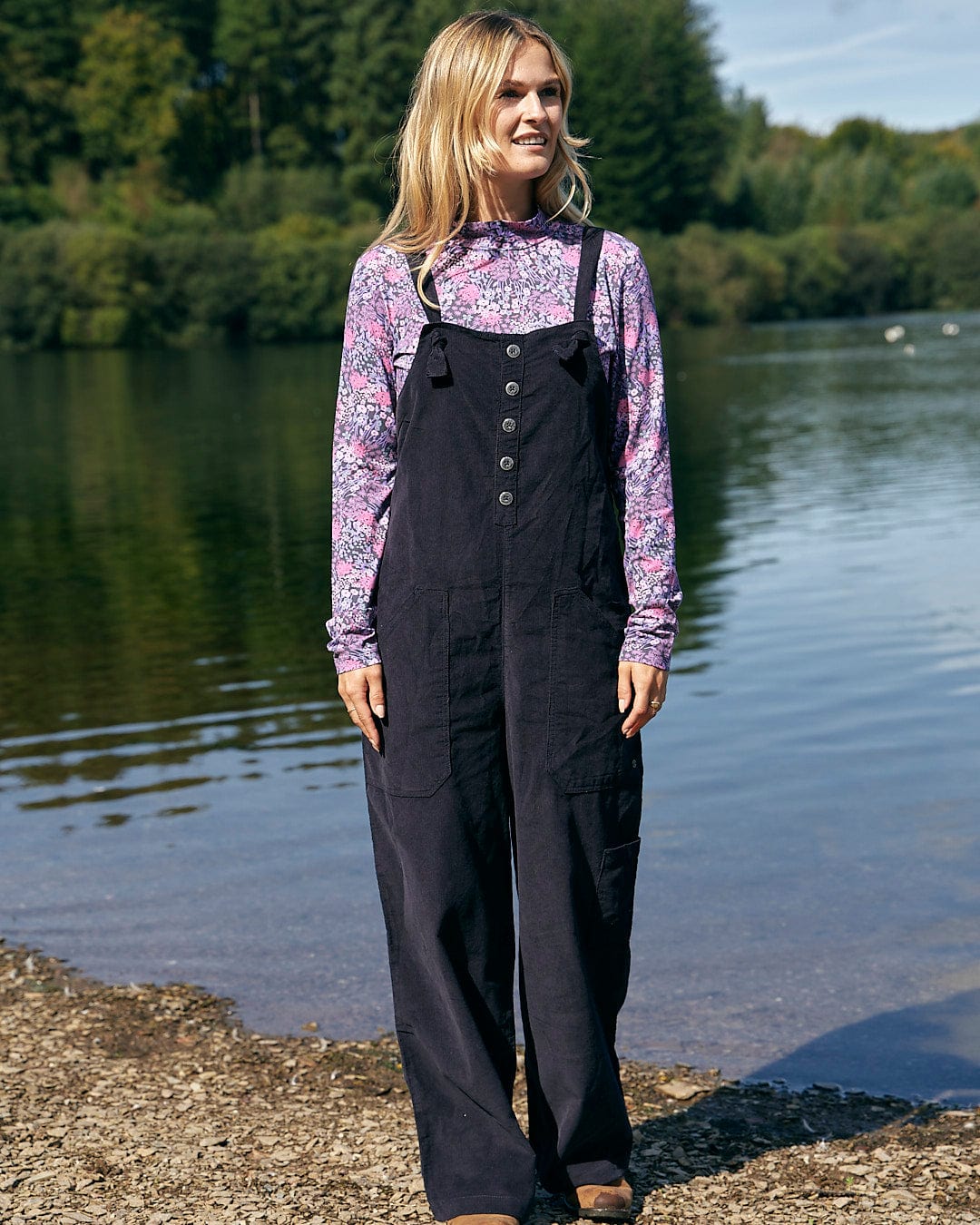 A stylish woman in comfortable Saltrock overalls standing by a lake.