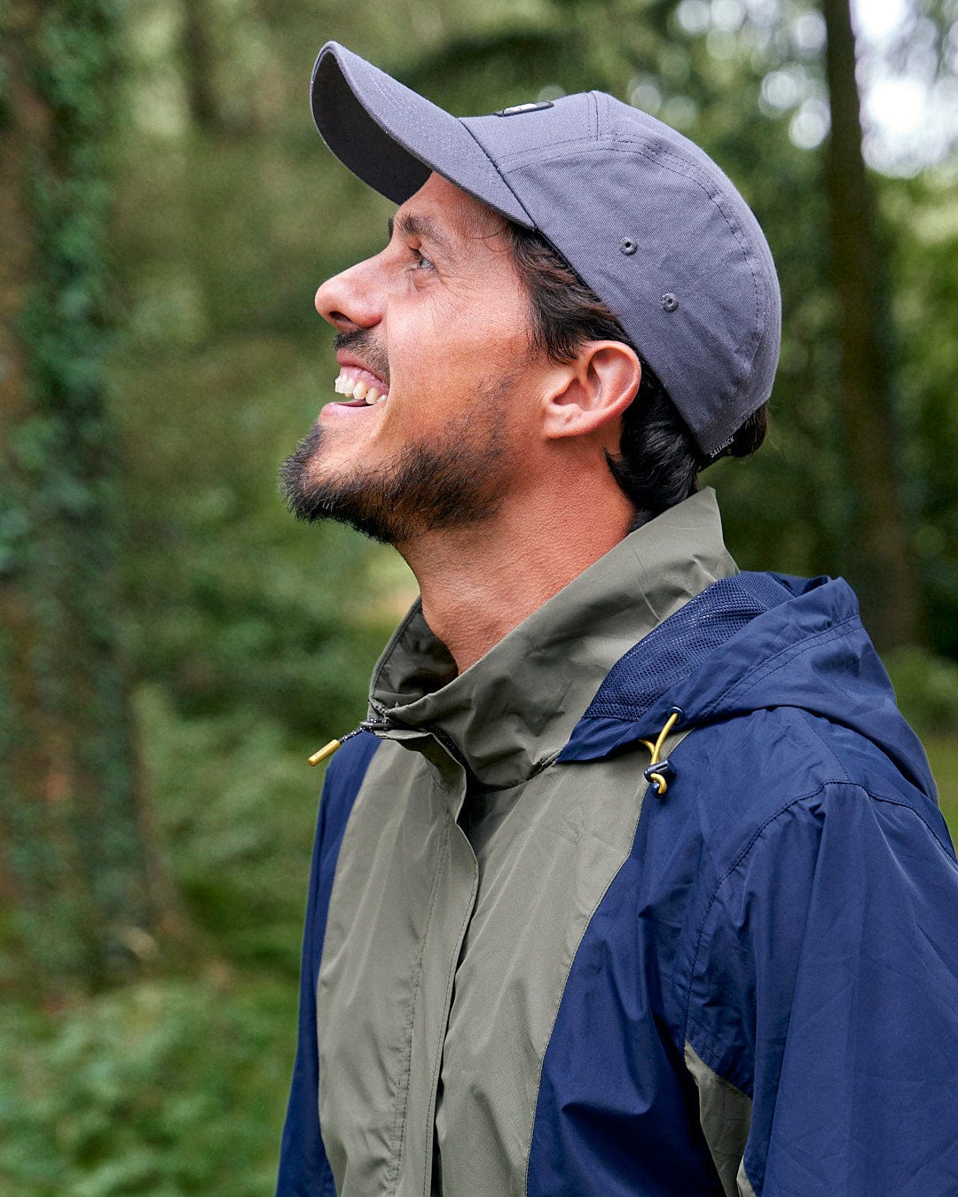 A man wearing a Saltrock Nevis - Mens Waterproof Mac - Blue/Green jacket and hat in the woods.