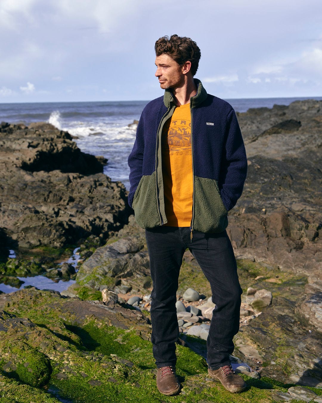 A man is standing in a field wearing a Saltrock Odin - Mens Zip Thru Fleece - Dark Blue jacket.