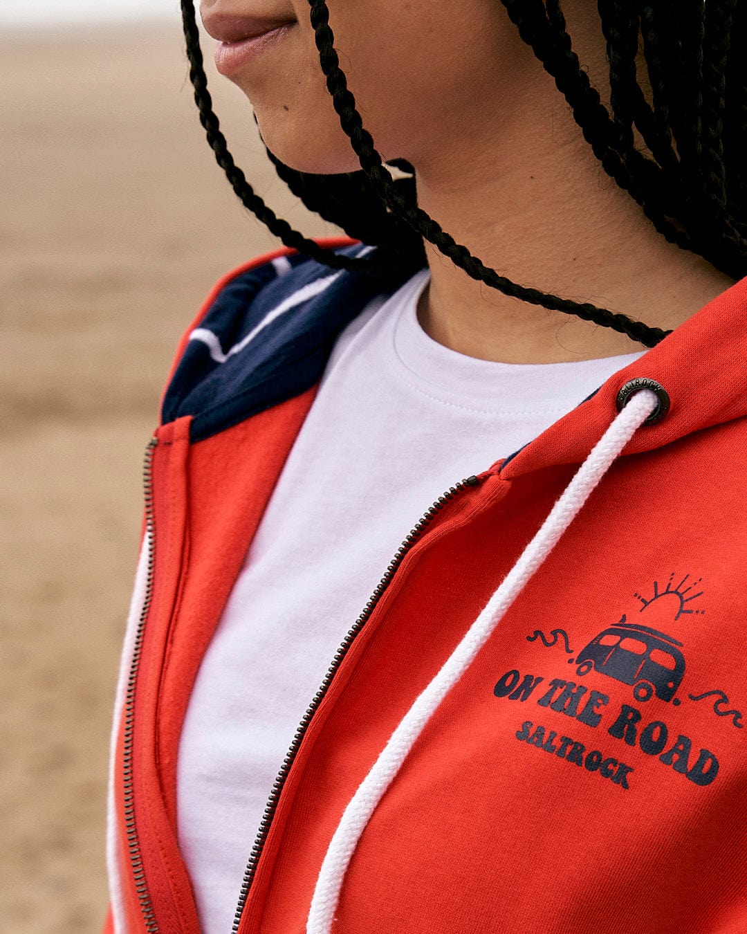 A black woman wearing a Saltrock On The Road Wales - Women's Zip Hoodie - Red on the beach.