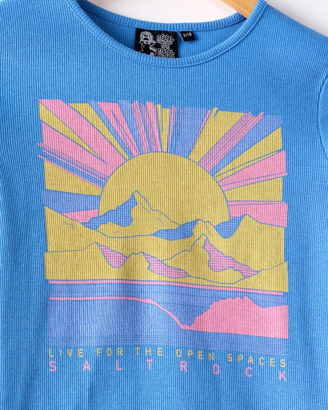 The Open Spaces Kids Long Sleeve T-Shirt by Saltrock is a blue slim-fit ribbed top, featuring a pastel mountain, sun, and rays illustration with "LIVE FOR THE OPEN SPACES SALTROCK" printed at the bottom.