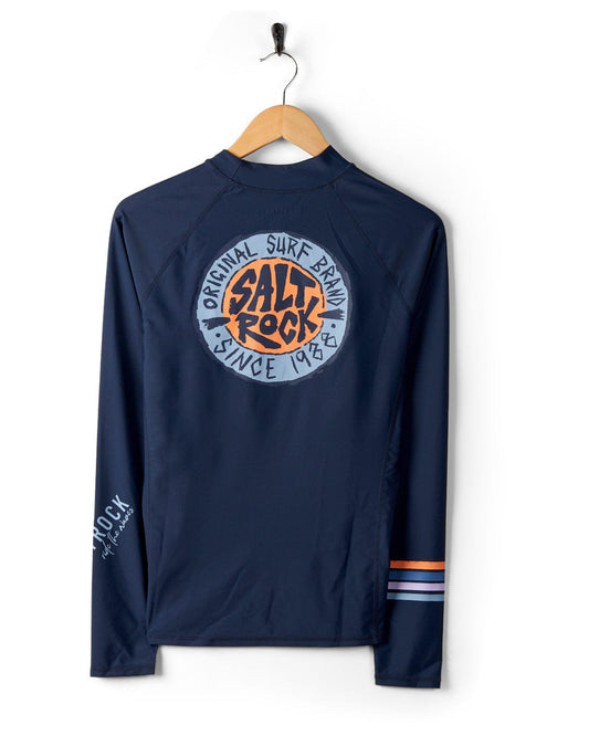 Navy blue long-sleeve rash guard with UPF 50 protection and "Saltrock original surf brand since 1978" logo on the back, hanging on a wooden hanger against a