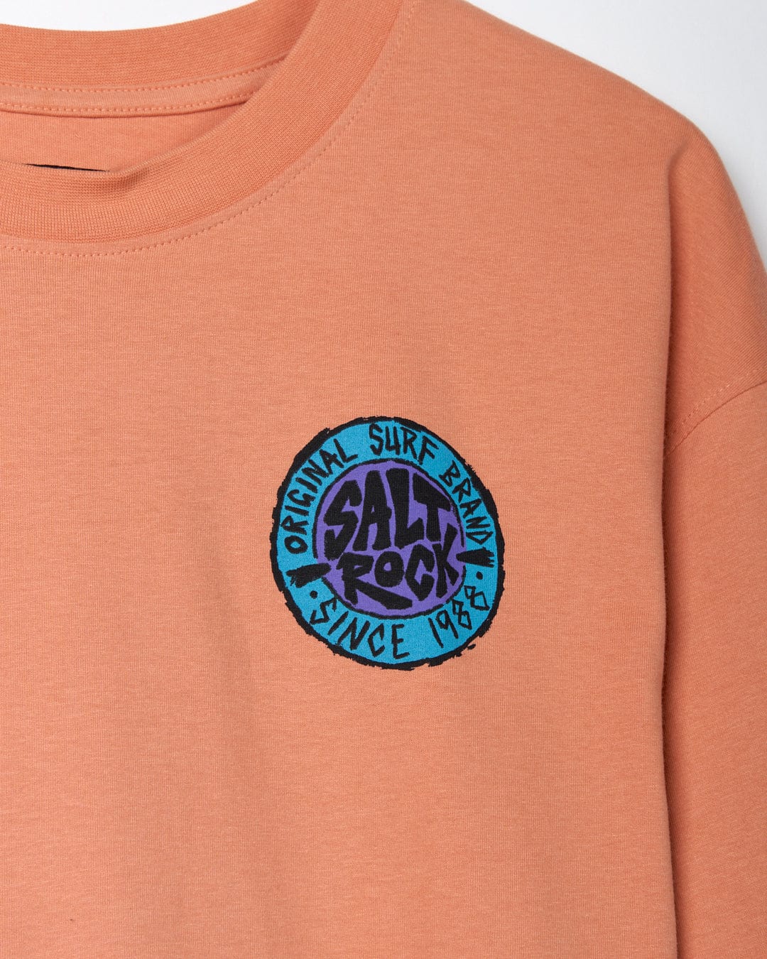 Close-up of an oversized peach-colored Saltrock t-shirt with a circular "SR Originals" logo patch on the chest.