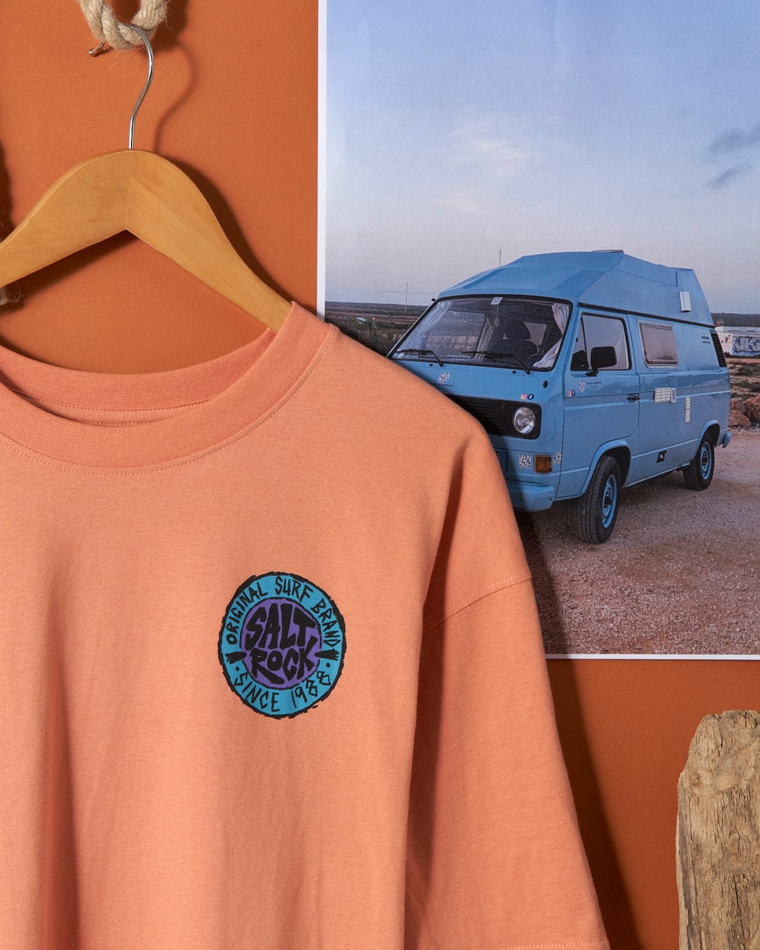 Saltrock salmon-colored oversized t-shirt with "Saltrock retro surf graphic" emblem hanging in front of a camper van photograph.