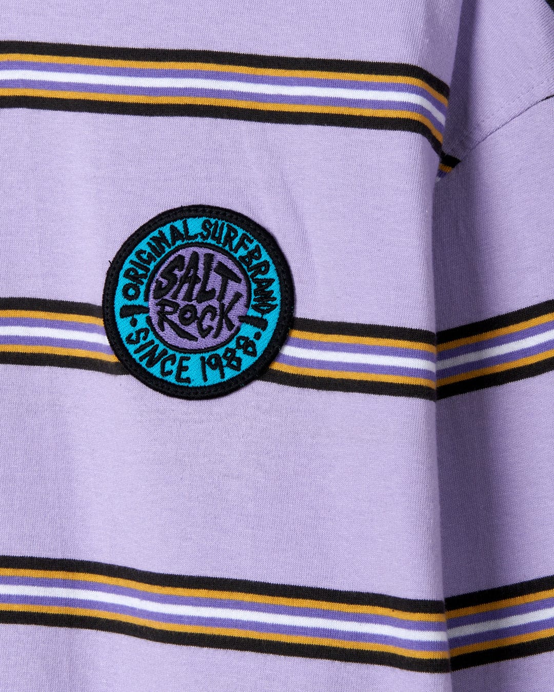 Close-up of a striped, cotton garment with an embroidered retro surf badge reading "SR Original surf brand Saltrock since 1988".