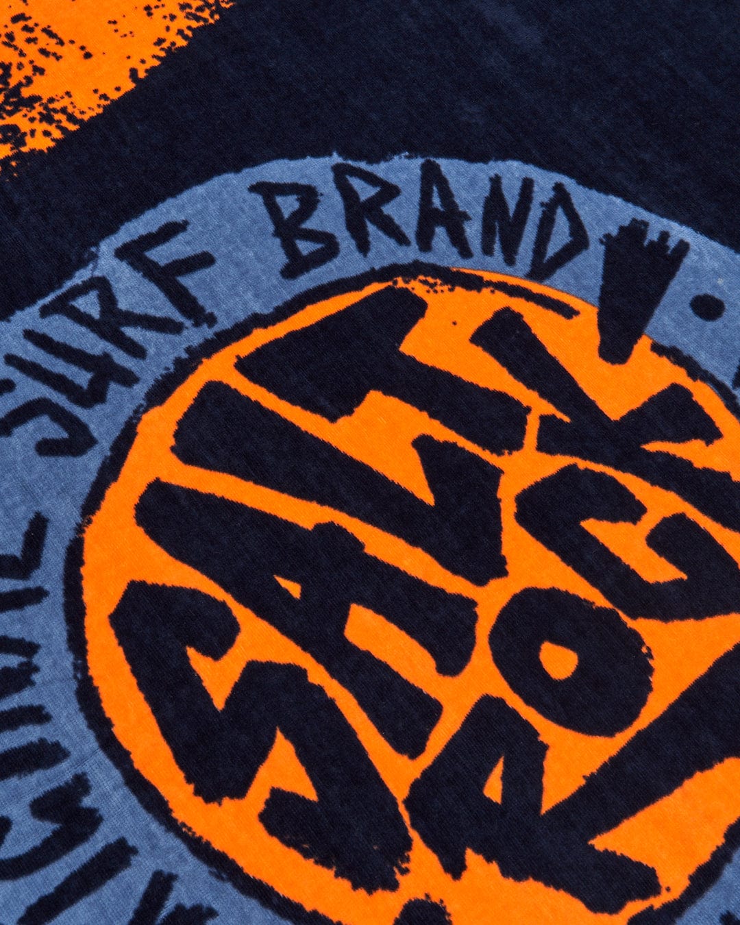 Close-up of a soft SR Original Towel Blue with a graphic print featuring the phrases "off the wall" and "off the wall brand" around a stylized orange and black circle logo with Saltrock branding.