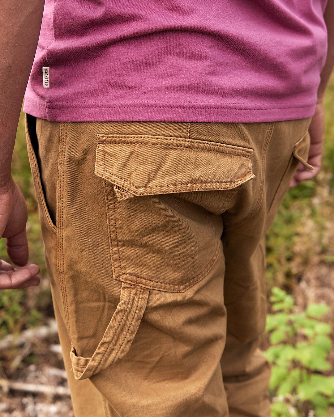 A man is standing in the woods wearing Saltrock Oslo Mens Carpenter Trouser in Brown.