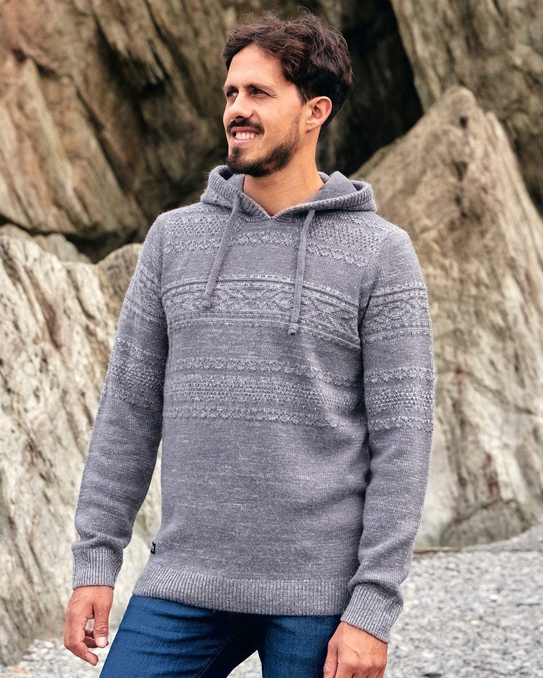 Saltrock - A man wearing a comfortable Paxton - Mens Knitted Hoodie - Grey standing on a rock.