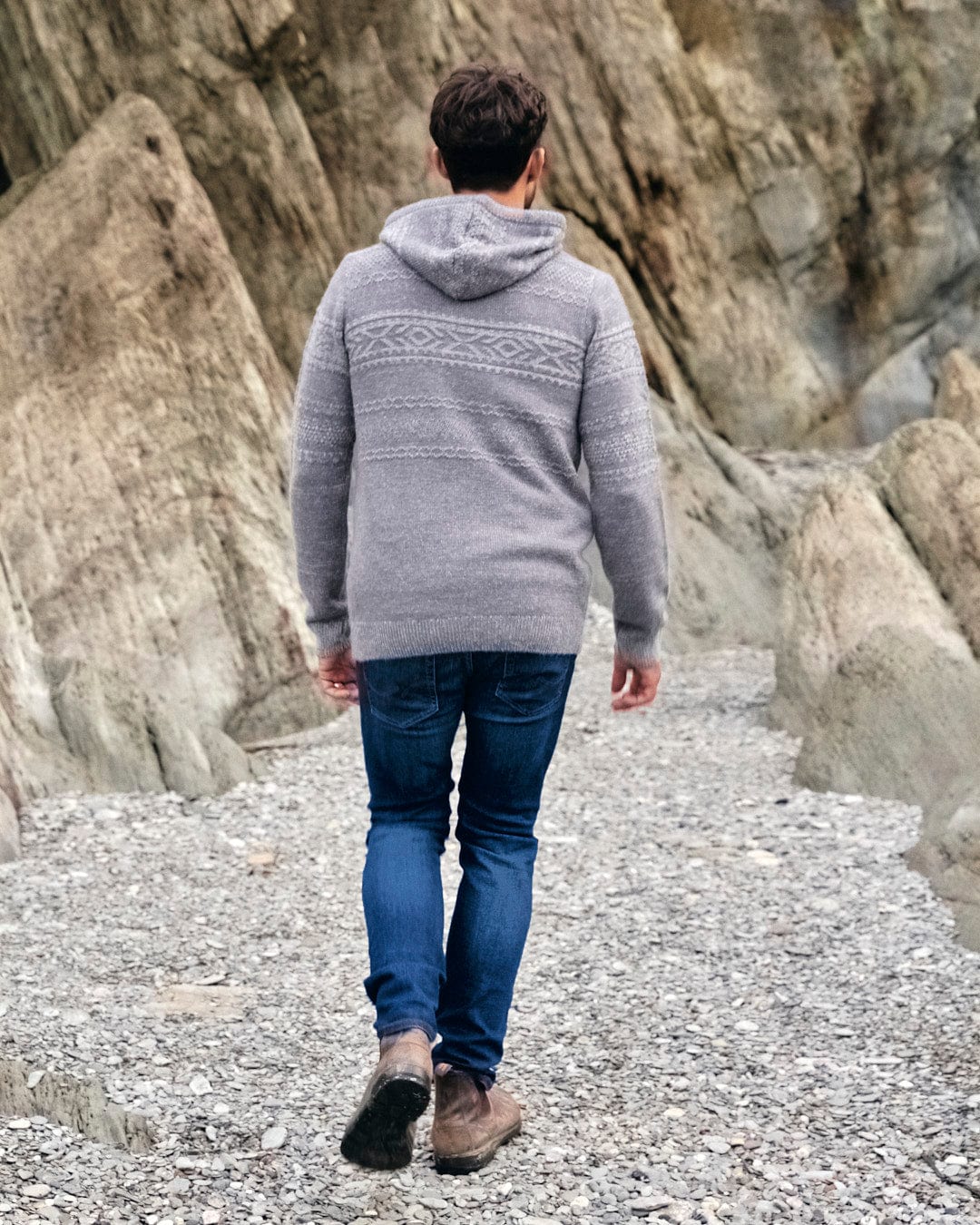 A man wearing a comfortable Saltrock Paxton - Mens Knitted Hoodie - Grey and jeans walking down a rocky path.