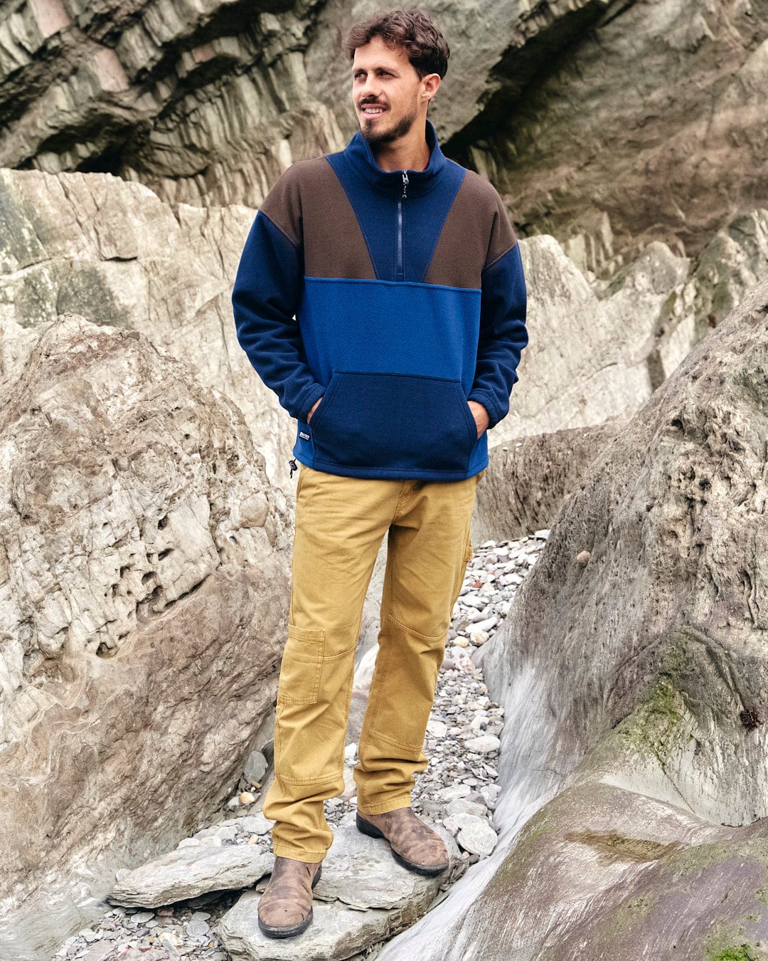 A man showcasing his style in a Saltrock Peninsula - Mens 1/4 Zip Pullover Fleece - Blue sweater while standing on rocks.