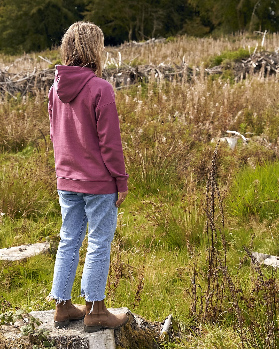 A girl in a Saltrock Pennie - Ladies Pop Hoodie - Dark Pink standing on a rock in a field.