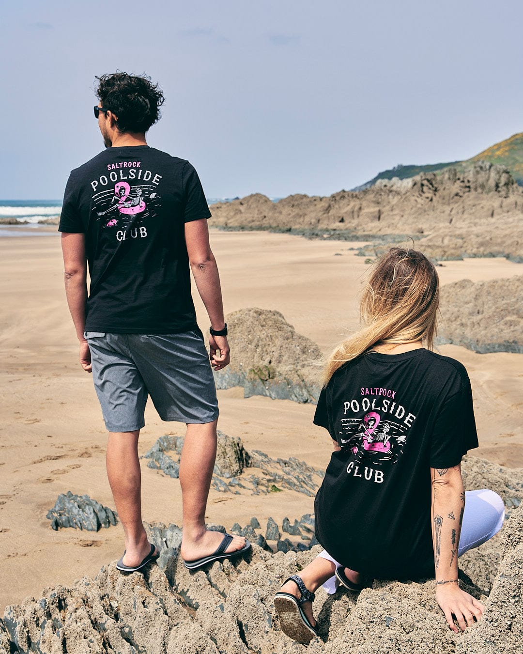 Two people sitting on rocks on the beach wearing Saltrock's Poolside Club Mens Short Sleeve T-Shirt in Black.